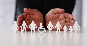 A person holds a paper cutout representing individuals with disabilities, symbolizing inclusivity and support.